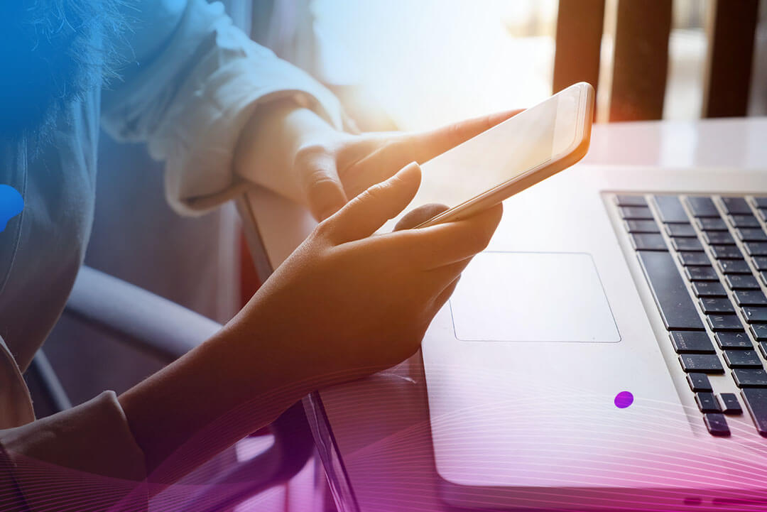 person holding their mobile phone in front of a laptop computer.